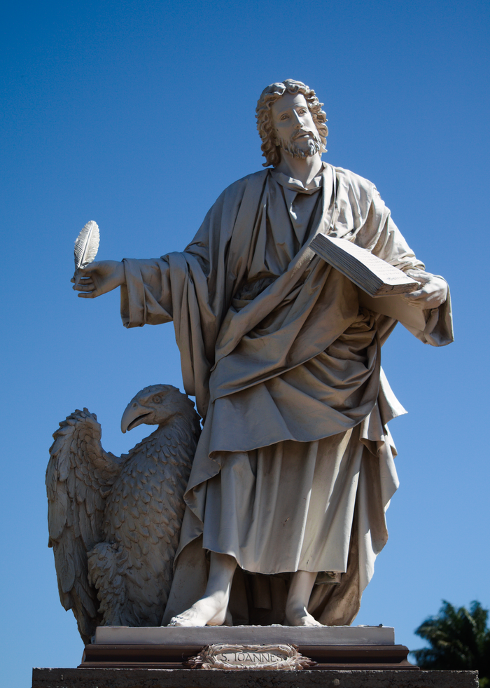 Marble statue of Saint John the Evangelist with an eagle under a clear blue sky.